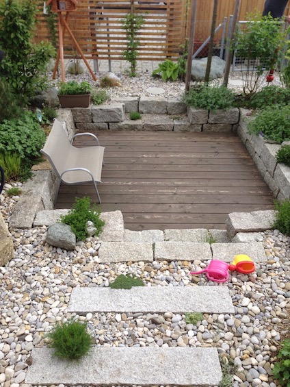 Die extrem kleine Gartenfläche wurde mit einem Holzdeck am Haus, einem kleinen versenkten Sitzplatz im hinteren Bereich sowie einer Bepflanzung mit Gehölzen und Stauden in Kiesbeeten sehr abwechslungsreich. (Poing bei München)