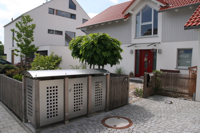 Mülltonnenhäuschen aus Edelstahl, Trompetenbaumkugeln im Hintergrund.  (München)